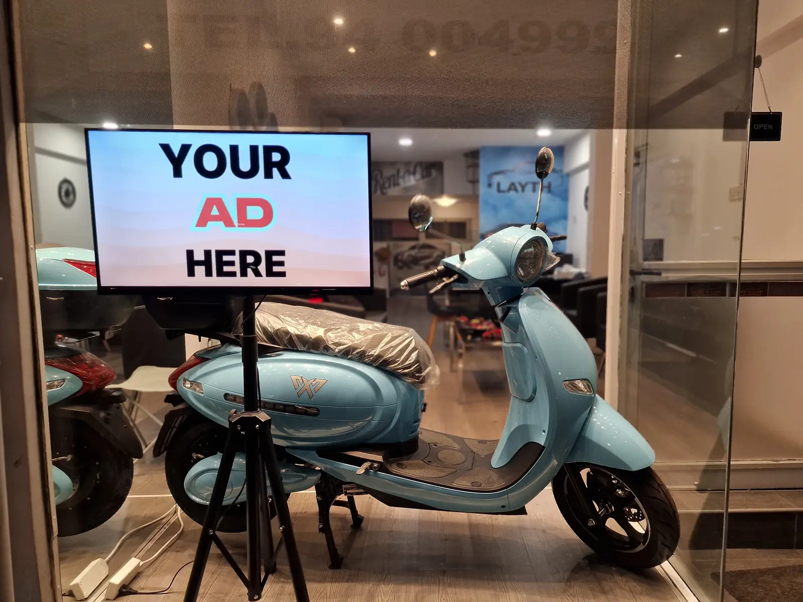 A shop window in Larnaca with an AdCoral screen showing “Your ad here”